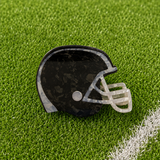 A football helmet-shaped hair claw with a black and gray marbled pattern and a translucent white faceguard, resting on green artificial turf.