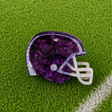 A purple football helmet-shaped hair claw with a white faceted face guard, resting on green artificial turf.
