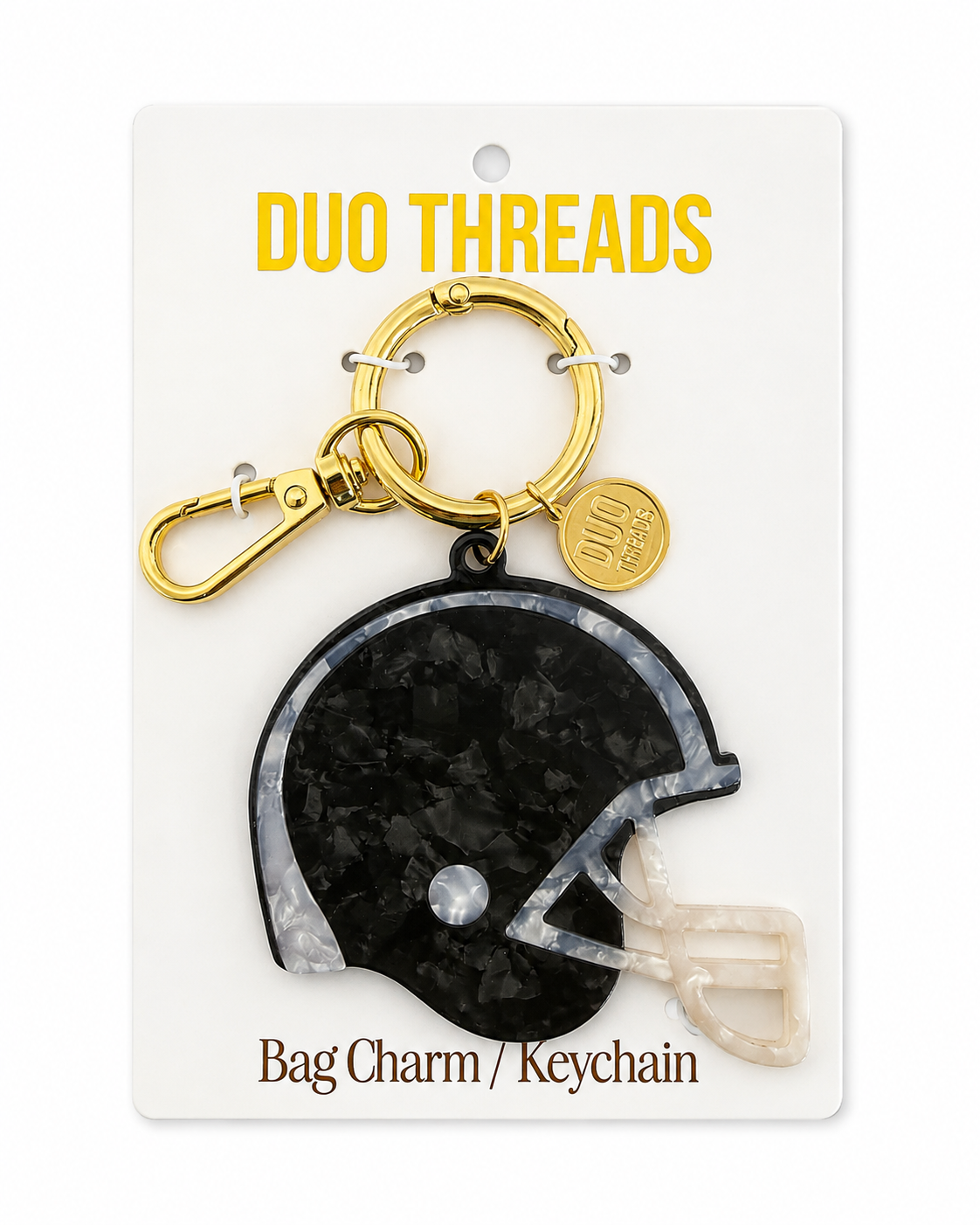 A football helmet-shaped bag charm keychain by Duo Threads, featuring a black and white patterned helmet charm with a gold clasp and a small gold brand tag, mounted on a white backing card.