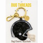 A football helmet-shaped bag charm keychain by Duo Threads, featuring a black and white patterned helmet charm with a gold clasp and a small gold brand tag, mounted on a white backing card.