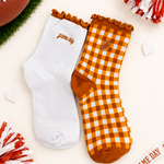 Two decorative ankle socks displayed on a light cream background with football-themed props. One sock is solid white with 'game day' embroidered in brown near the cuff.