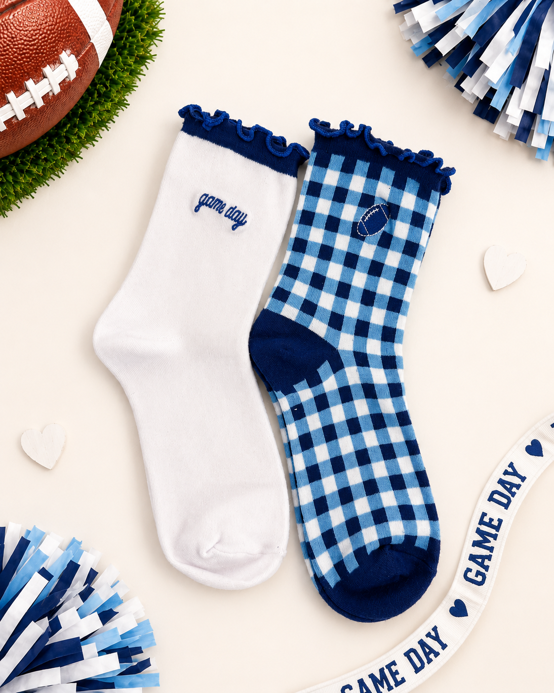 Two pairs of women's crew socks styled in a flat-lay arrangement. One pair is solid white with a navy blue ruffled cuff and 'game day' text on the side.