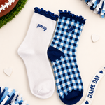 Two pairs of women's crew socks styled in a flat-lay arrangement. One pair is solid white with a navy blue ruffled cuff and 'game day' text on the side.