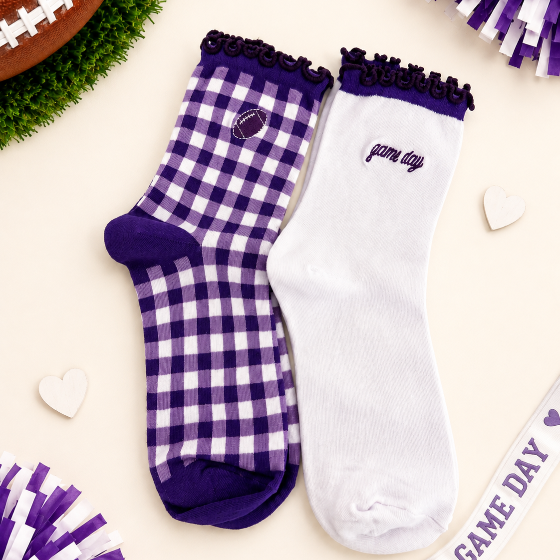 Two decorative ankle socks displayed on a cream background with football-themed props. One sock is white with a purple gingham check pattern, purple trim, and a small football patch near the cuff.