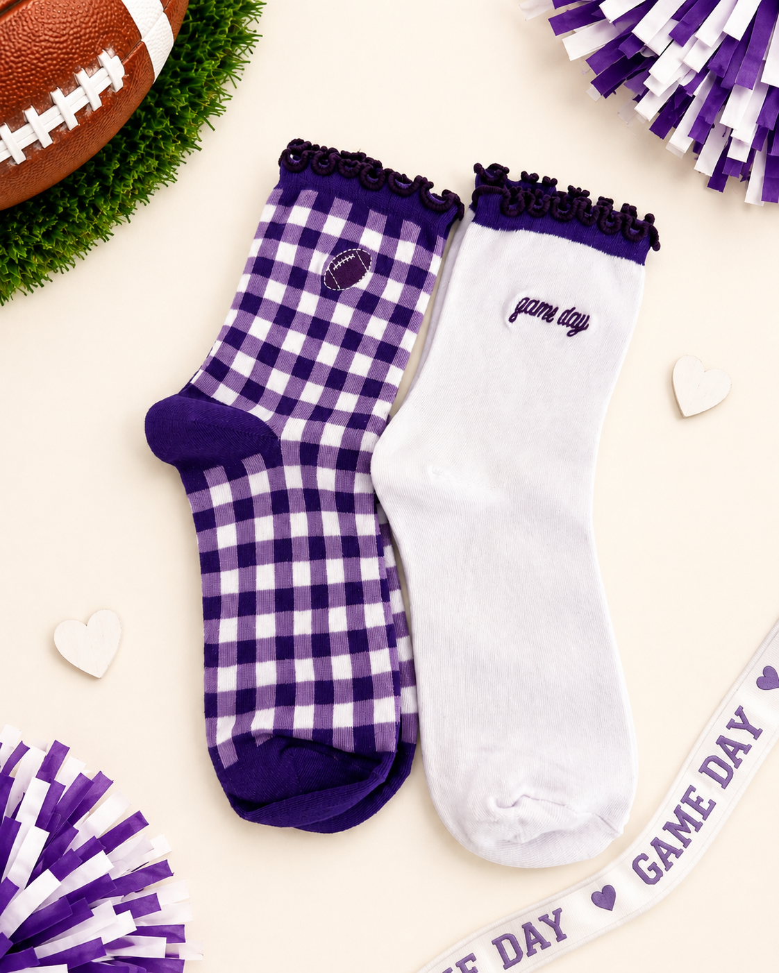 Two decorative ankle socks displayed on a cream background with football-themed props. One sock is white with a purple gingham check pattern, purple trim, and a small football patch near the cuff.