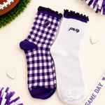 Two decorative ankle socks displayed on a cream background with football-themed props. One sock is white with a purple gingham check pattern, purple trim, and a small football patch near the cuff.