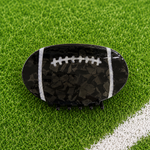 A football-shaped hair claw clip with a glossy black and dark gray marbled pattern, white laces, and white side stripes, displayed on a green turf background