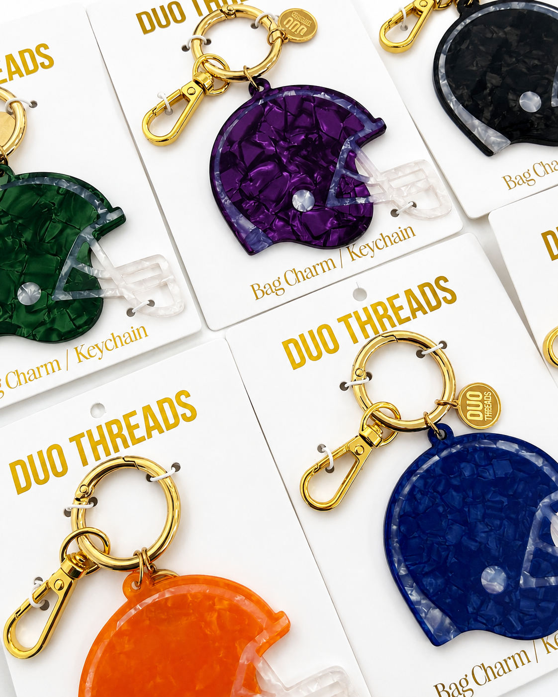 Several football helmet-shaped bag charms and keychains on white cards, each with gold clasp hardware. Visible colors include green, purple, orange, and blue, with the brand name DUO THREADS printed on the cards.