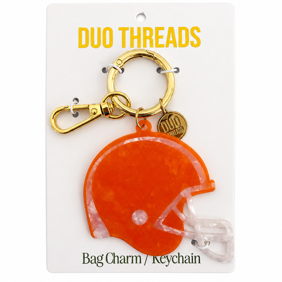 An orange helmet-shaped bag charm keychain by Duo Threads, attached to a gold clasp and a small round gold tag, displayed on a white backing card.