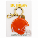 An orange helmet-shaped bag charm keychain by Duo Threads, attached to a gold clasp and a small round gold tag, displayed on a white backing card.
