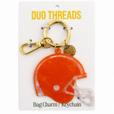 An orange helmet-shaped bag charm keychain by Duo Threads, attached to a gold clasp and a small round gold tag, displayed on a white backing card.