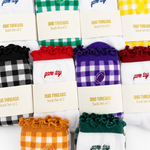 Eight pairs of sock sets arranged in a grid, each with a branded cream paper sleeve reading 'DUO THREADS Sock Set of 2'. The socks feature different colorways including green-and-white gingham, blue-and-white gingham, yellow-and-white gingham, black-and-white gingham, red-and-white gingham, purple-and-white gingham, orange-and-white gingham, and dark green-and-white gingham.
