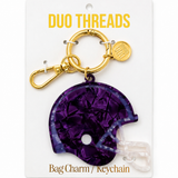 A purple football helmet bag charm keychain by Duo Threads, attached to a gold-tone split ring and clasp, displayed on its white backing card.