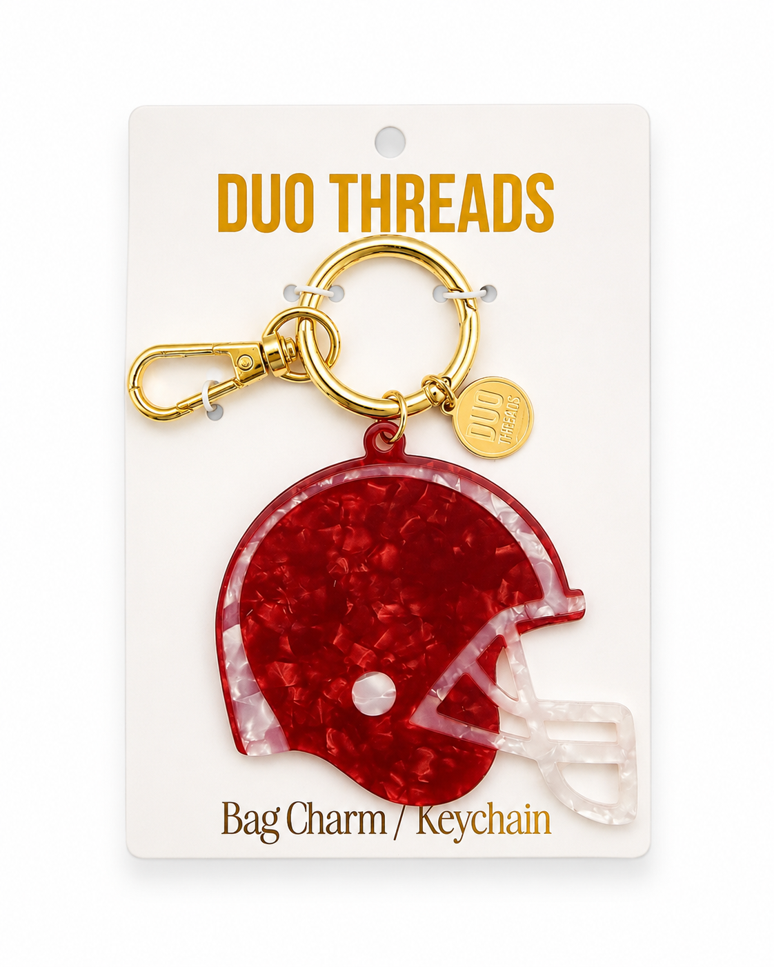 A red glitter football helmet bag charm keychain by Duo Threads, attached to a gold clasp and displayed on its white retail backing card.