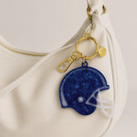 Video flipping through the varying colors of helmet shaped bag charms clipped to a white slouchy purse with gold hardware.