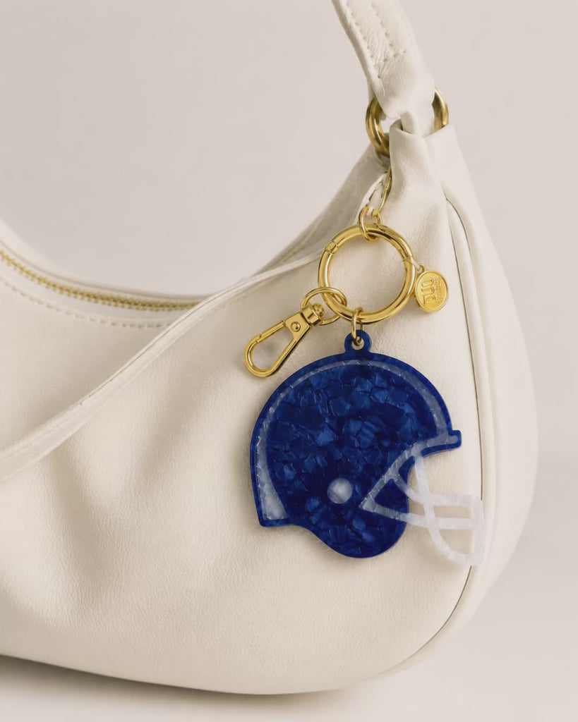 Video flipping through the varying colors of helmet shaped bag charms clipped to a white slouchy purse with gold hardware.